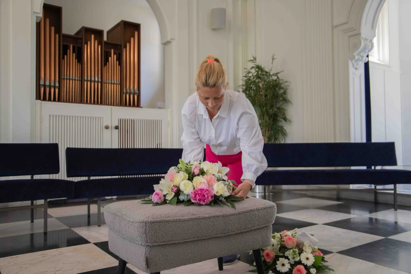 Een uitvaartbegeleider legt bloemen klaar in een aula