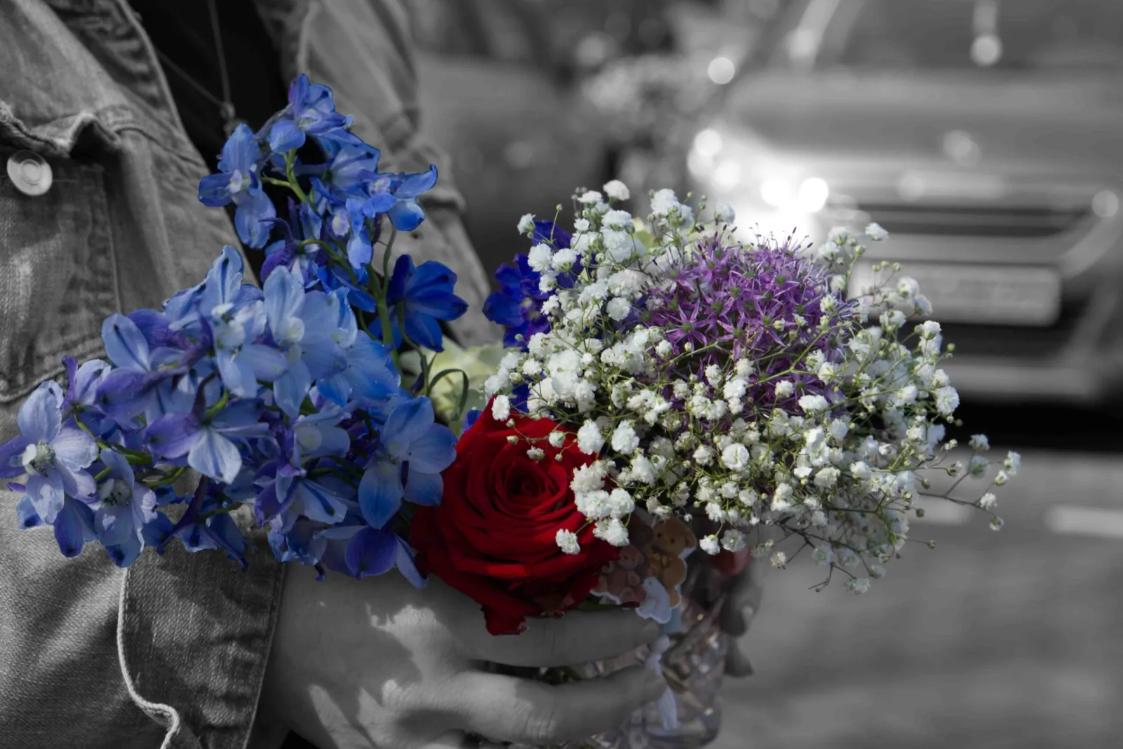 Iemand houdt een boeket vast met blauwe ridderspoor, een rode roos en gipskruid